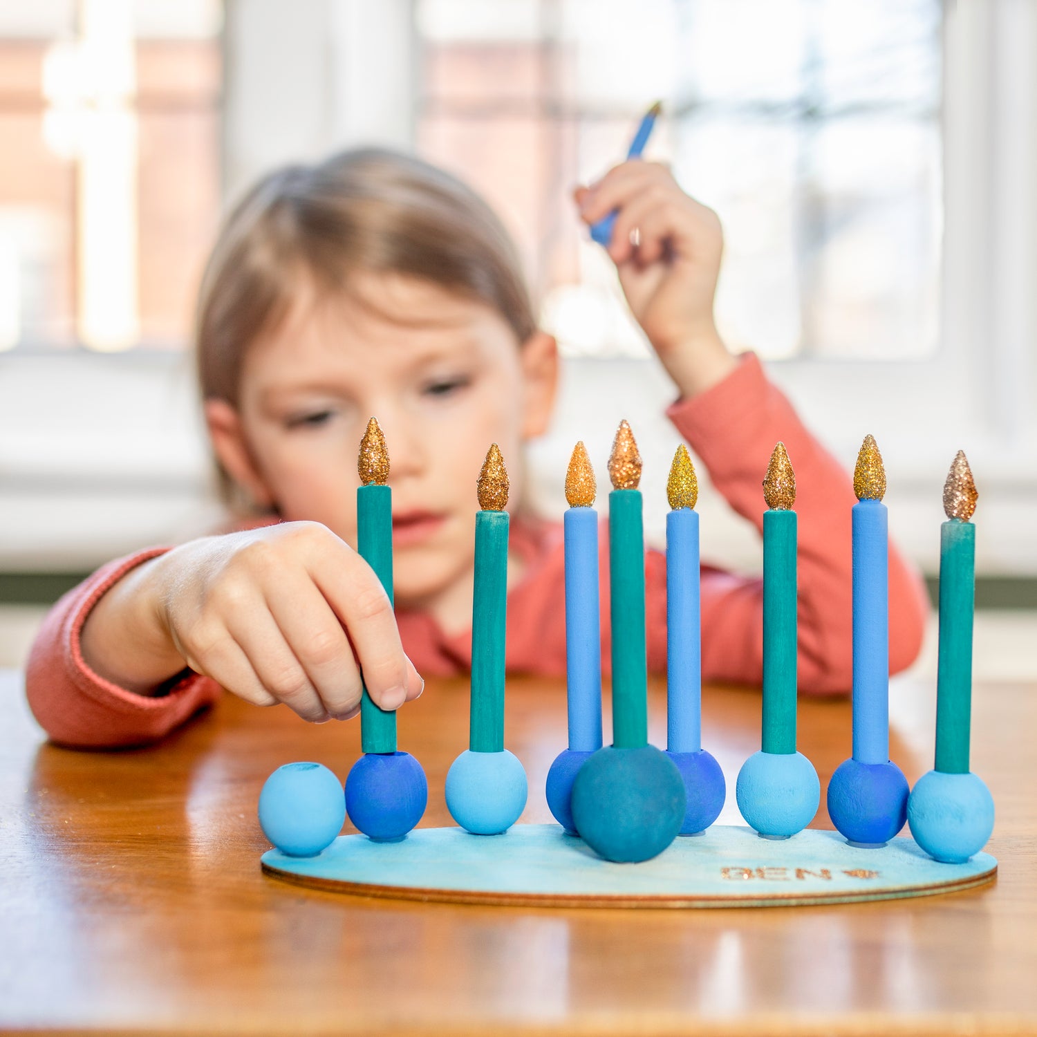 "Hanukkah gift ideas: Explore our collection of thoughtful presents for the holiday season. ALT: Child playing with self-made wooden play menorah, embodying the joy of Hanukkah."